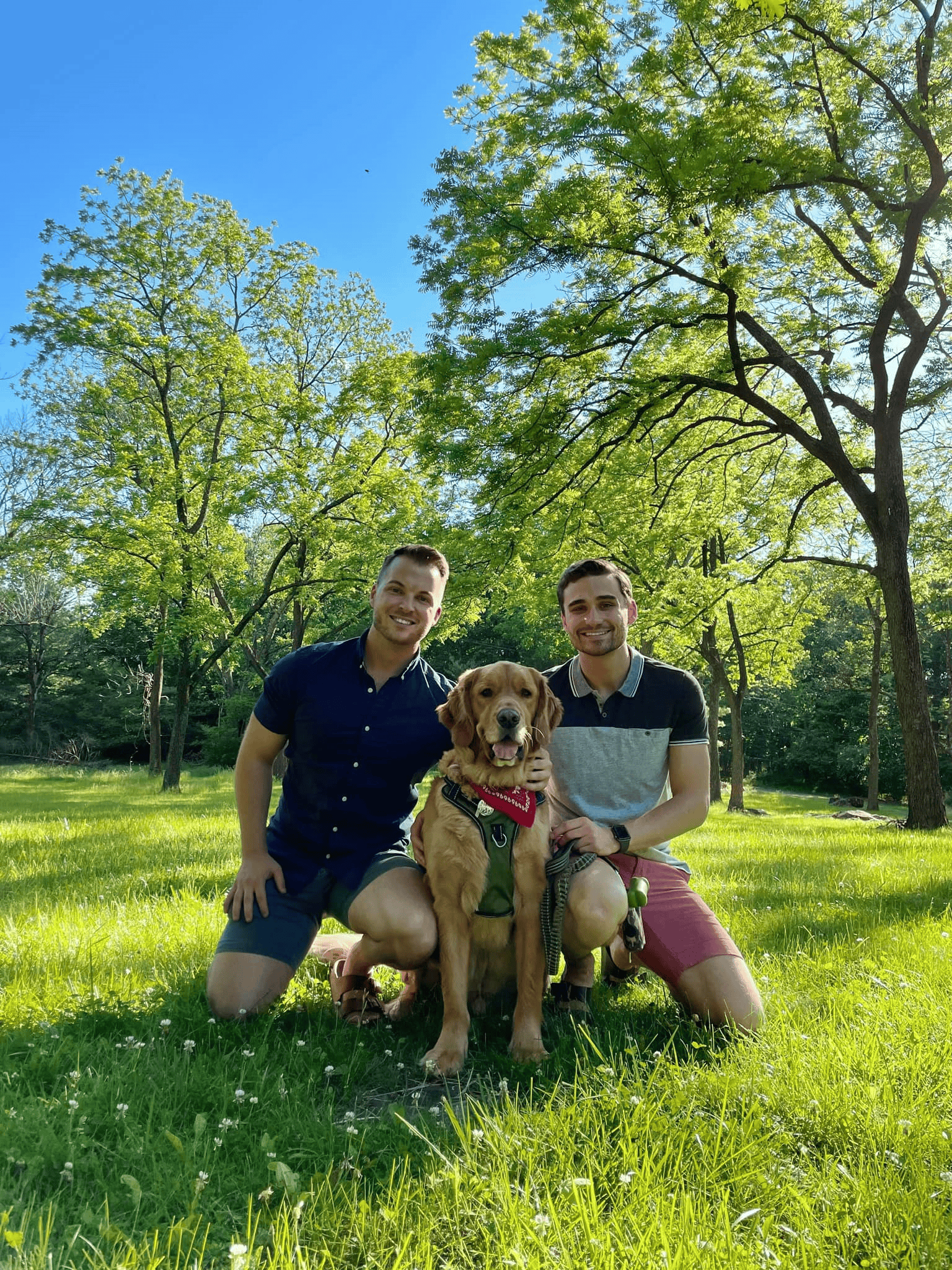 two young men and their dog kneeling in an outdoor setting